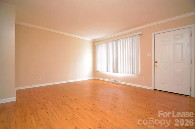 an empty room with wooden floor and windows with curtains