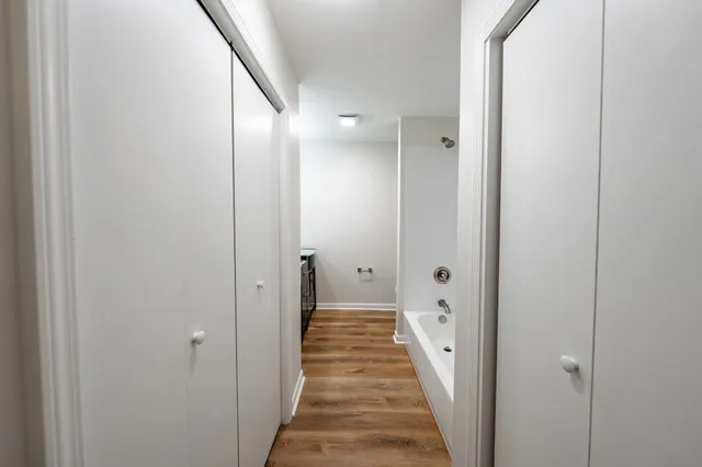 a view of a hallway with wooden floor and a bathroom