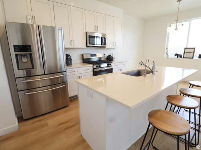 8240 Cascade Vw Way Magna, UT 84044 - Photo 4 of 18 Kitchen with stainless steel appliances, a kitchen breakfast bar, an island with sink, light wood finished floors, and white cabinets