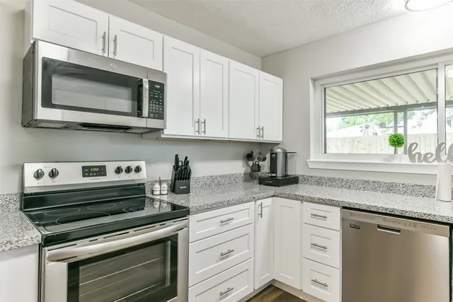 a kitchen with granite countertop white cabinets appliances and a window