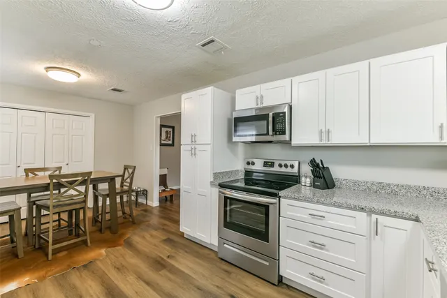 a kitchen with stainless steel appliances granite countertop a stove a sink a refrigerator a dining table and chairs with wooden floor