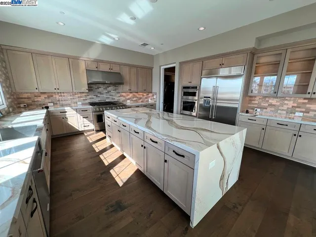 a kitchen with stainless steel appliances granite countertop a stove top oven a sink dishwasher a refrigerator and white cabinets with wooden floor
