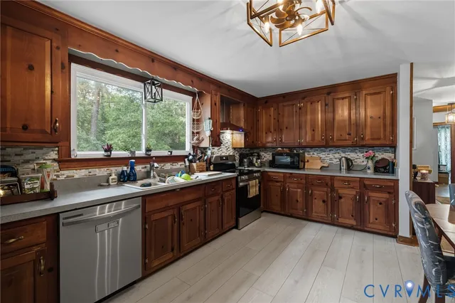 a kitchen with stainless steel appliances granite countertop wooden cabinets a stove a sink and dishwasher with wooden floor