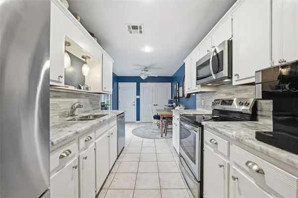 a kitchen with stainless steel appliances granite countertop a stove top oven a sink dishwasher a refrigerator and white cabinets with wooden floor