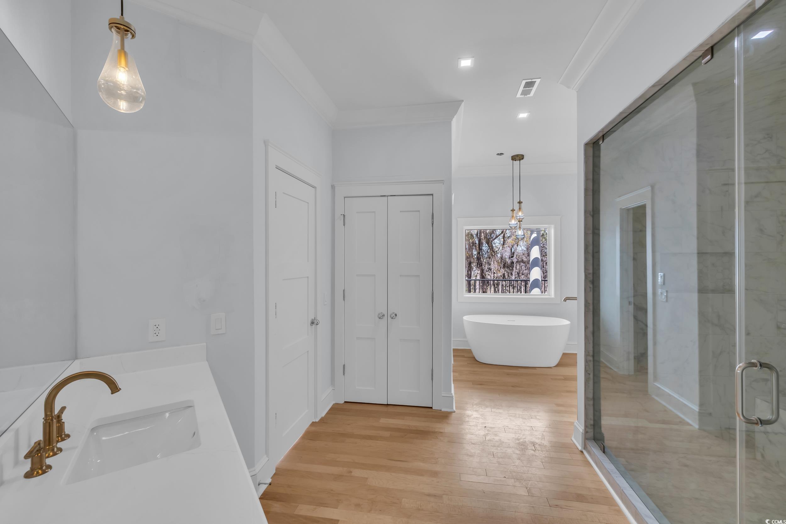 511 Rice Bluff Road Pawleys Island, SC 29585 - Photo 21 of 40 Bathroom with a freestanding tub, crown molding, a sink, wood finished floors, and visible vents