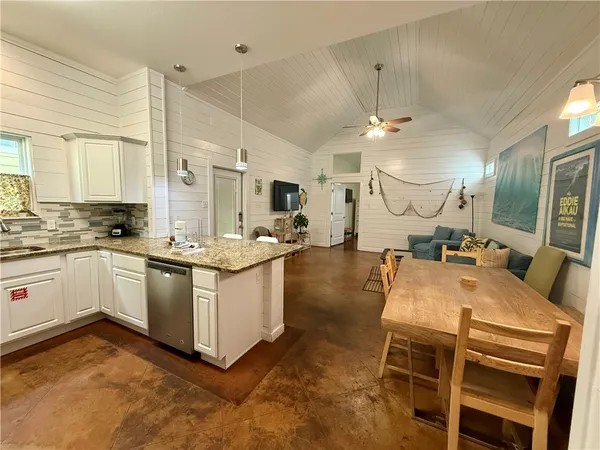 a kitchen with stainless steel appliances kitchen island granite countertop a sink dishwasher a stove a dining table and chairs with wooden floor