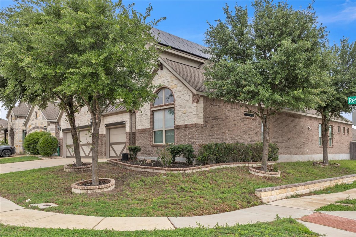 21301 Resource Road Pflugerville, TX 78660 - Photo 25 of 29 Brick and stone facade featuring a prominent arched window, two garage doors with decorative elements, and solar panels on the roof