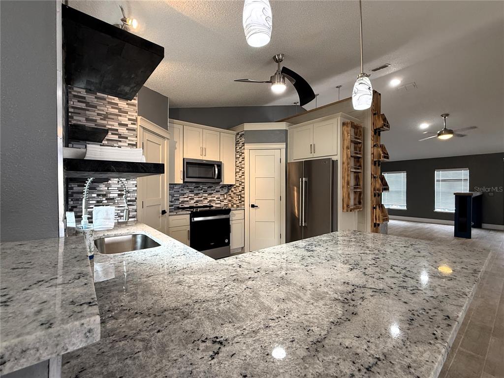 6172 Raleigh Street Spring Hill, FL 34606 - Photo 25 of 64 a large kitchen with stainless steel appliances kitchen island granite countertop a sink a stove and a refrigerator