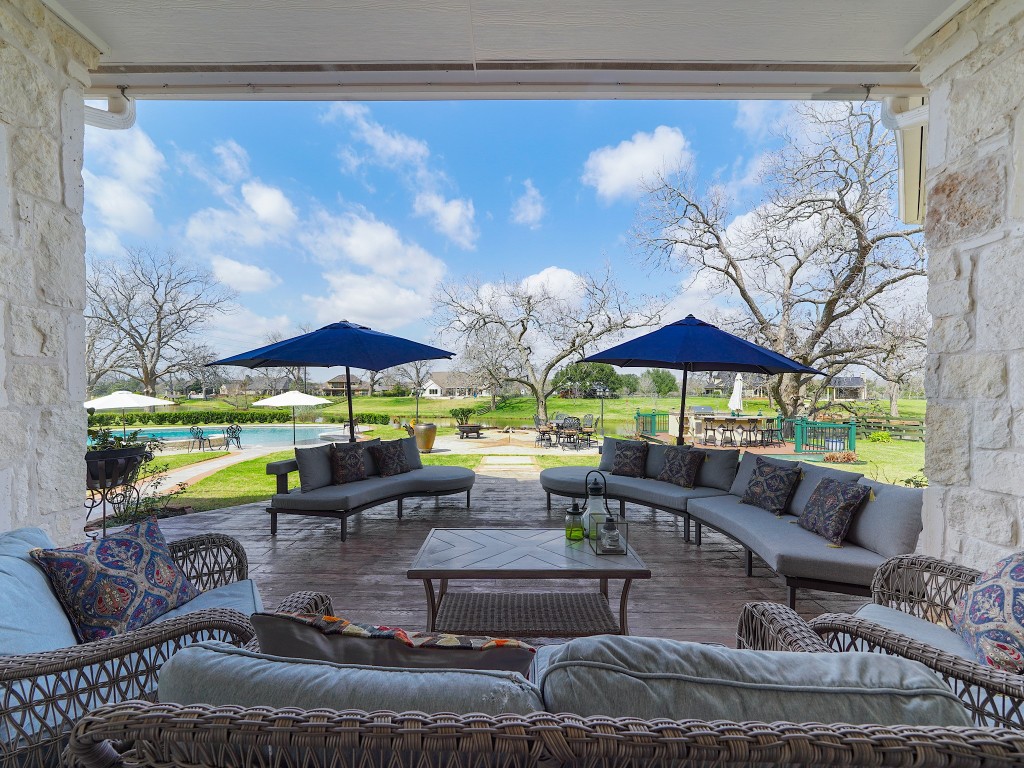 32134 Fulbrook Commons Fulshear, TX 77441 - Photo 42 of 49 Framed by wide openings, the covered patio offers panoramic views of the lawn, pool, and lake beyond — blending luxury living with tranquil natural surroundings.
