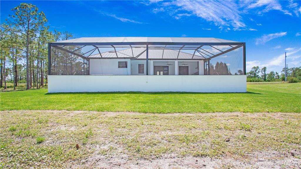 2343 Oil Well Road Naples, FL 34120 - Photo 30 of 46 Rear exterior featuring a large screened lanai, a white concrete privacy wall, and a metal roof