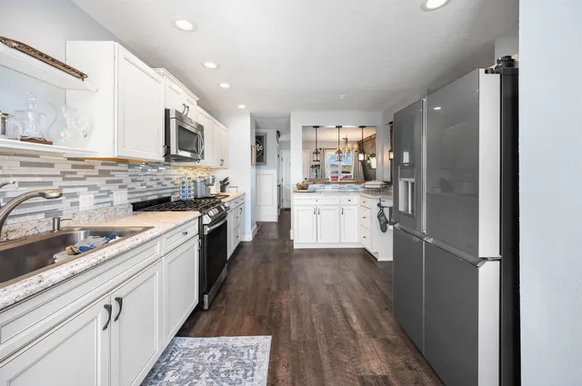 a kitchen with stainless steel appliances kitchen island granite countertop a stove top oven a sink a refrigerator white cabinets and wooden floor