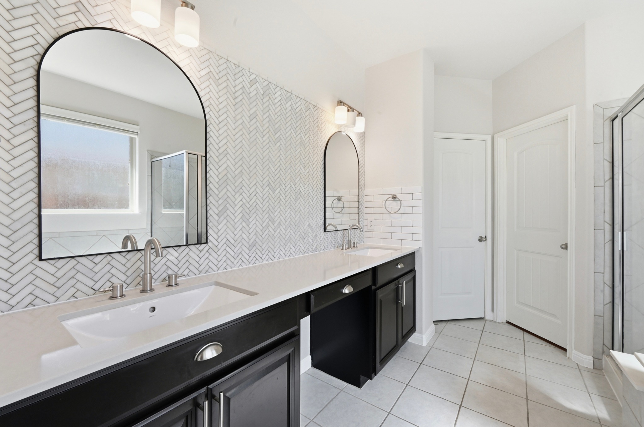 351 Wincliff Drive Buda, TX 78610 - Photo 23 of 40 Double vanities with sleek black cabinetry and herringbone tile create a refined and elegant bathroom space.