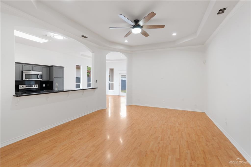 3315 Omega Street Edinburg, TX 78539 - Photo 2 of 19 Unfurnished living room with a ceiling fan, light wood-type flooring, arched walkways, recessed lighting, and a raised ceiling