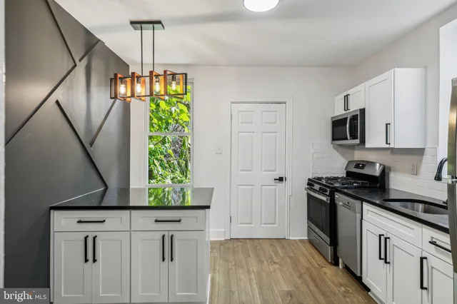 a kitchen with stainless steel appliances granite countertop a refrigerator a stove a sink dishwasher and white cabinets with wooden floor