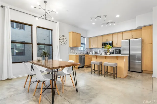 a kitchen with stainless steel appliances kitchen island granite countertop a refrigerator a stove top oven a sink a dining table and chairs with wooden floor
