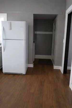 a view of a refrigerator in kitchen and an empty room with wooden floor