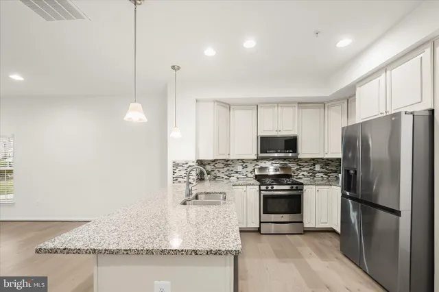 a kitchen with stainless steel appliances granite countertop a refrigerator a stove a sink and a oven with wooden floor