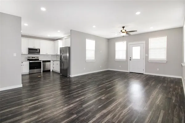 an empty room with wooden floor and kitchen view