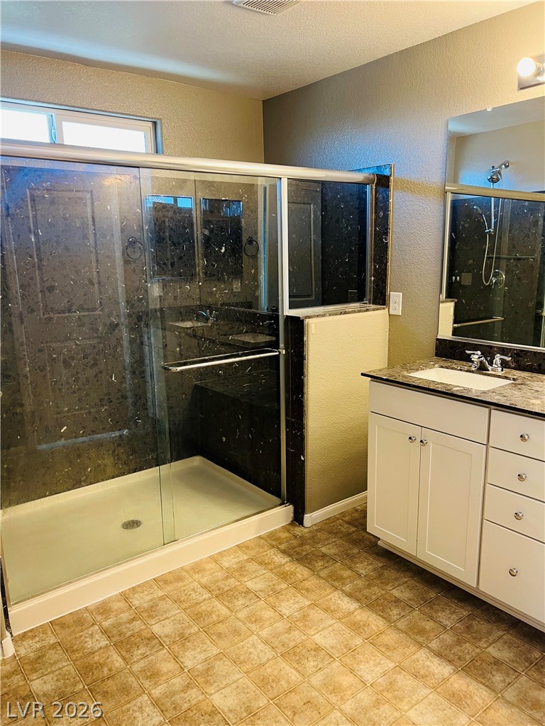 9325 Keystone Ridge Avenue Las Vegas, NV 89148 - Photo 8 of 17 A well-lit bathroom features a glass-enclosed shower and a vanity with a sleek countertop.