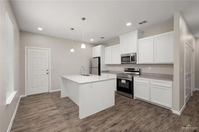 a kitchen with stainless steel appliances granite countertop a stove top oven a sink a refrigerator white cabinets and wooden floor