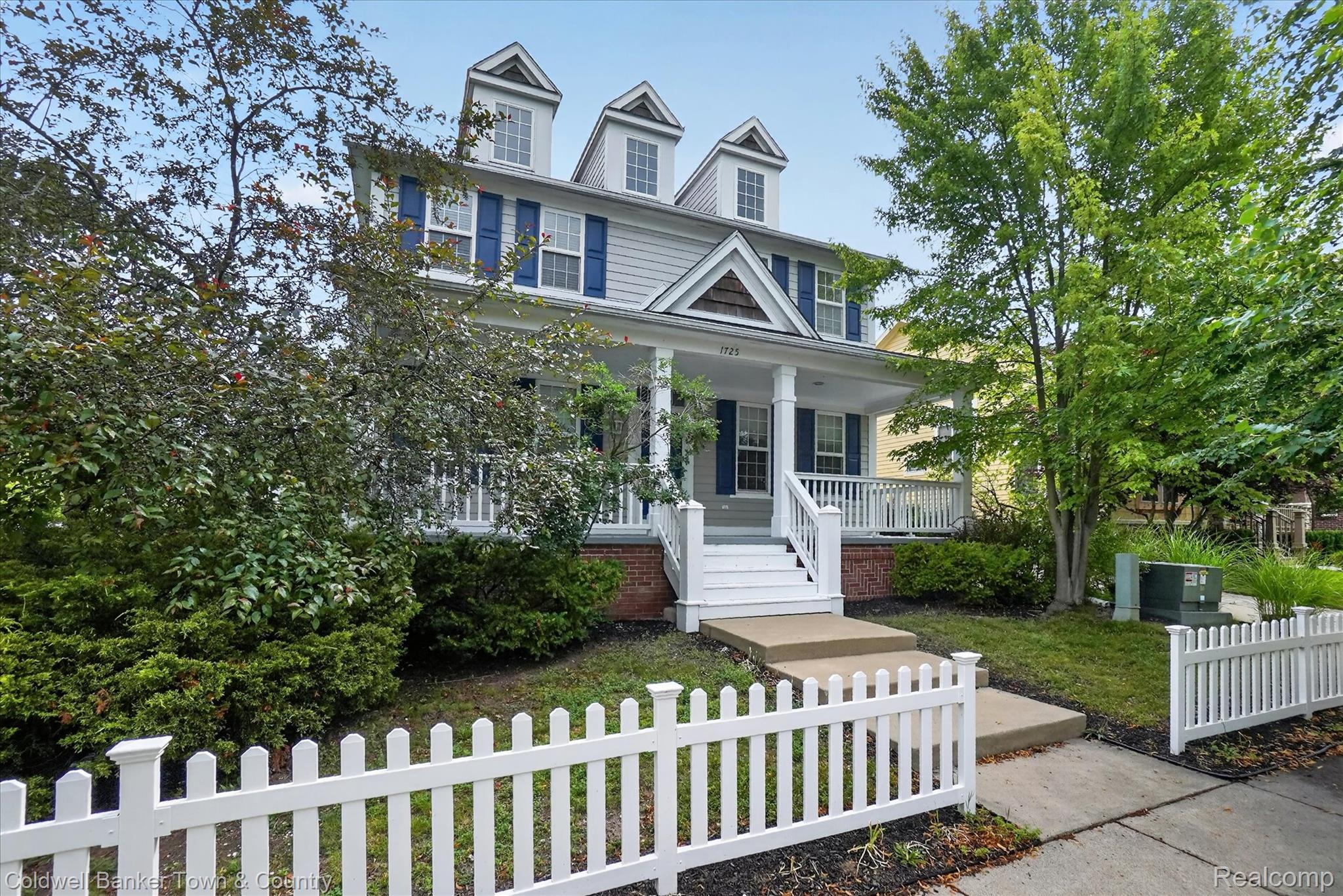 1725 Town Commons Drive Howell, MI 48855 - Photo 2 of 53 Traditional-style residence featuring a prominent front porch with white railings, a concrete pathway, and a white picket fence