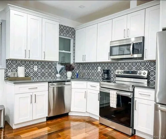 a kitchen with granite countertop white cabinets stainless steel appliances and wooden floor