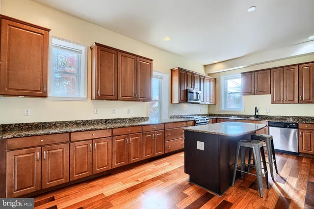 a kitchen with stainless steel appliances granite countertop wooden cabinets a stove top oven a sink and dishwasher with wooden floor