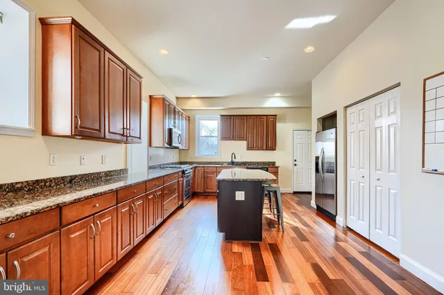 a kitchen with stainless steel appliances granite countertop a refrigerator a sink dishwasher a stove and a oven with wooden floor