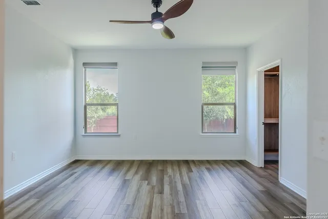 an empty room with wooden floor fan and windows