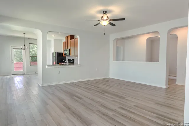 a view of an empty room with wooden floor and a kitchen