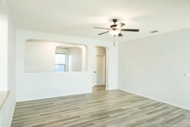 a view of an empty room with wooden floor and a ceiling fan