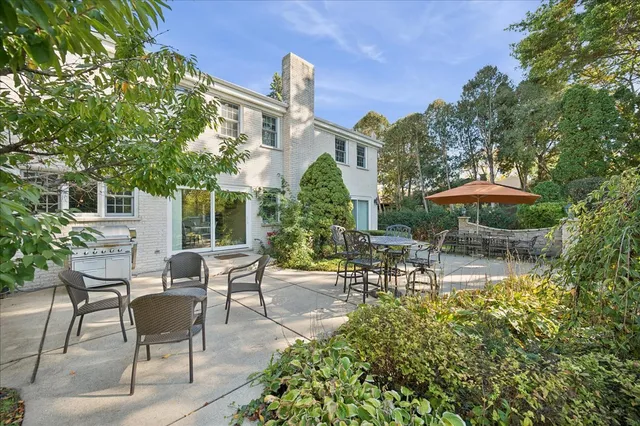 a view of a patio with table and chairs under an umbrella with large trees