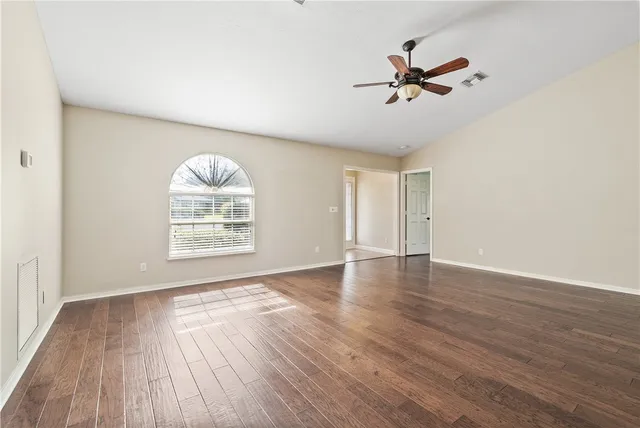 an empty room with wooden floor fan and windows