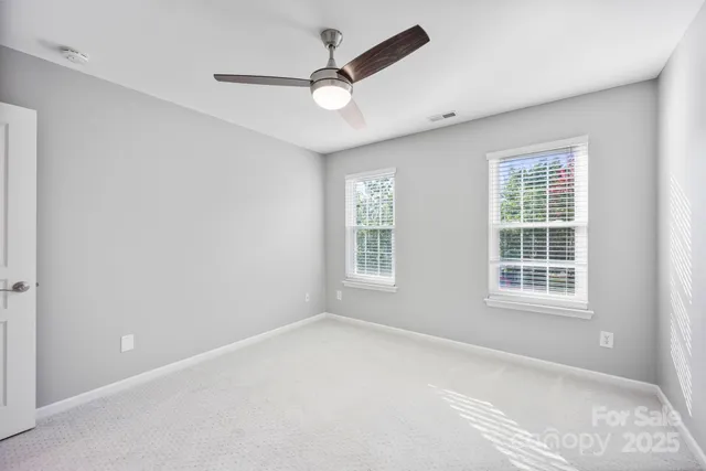 an empty room with ceiling fan and windows