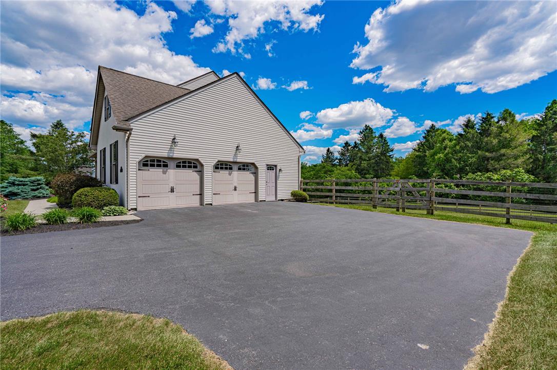 6000 Pond View Terrace Bath, PA 18014 - Photo 5 of 69 A spacious asphalt driveway leads to a two-car garage, framed by verdant landscaping and a rustic wooden fence.