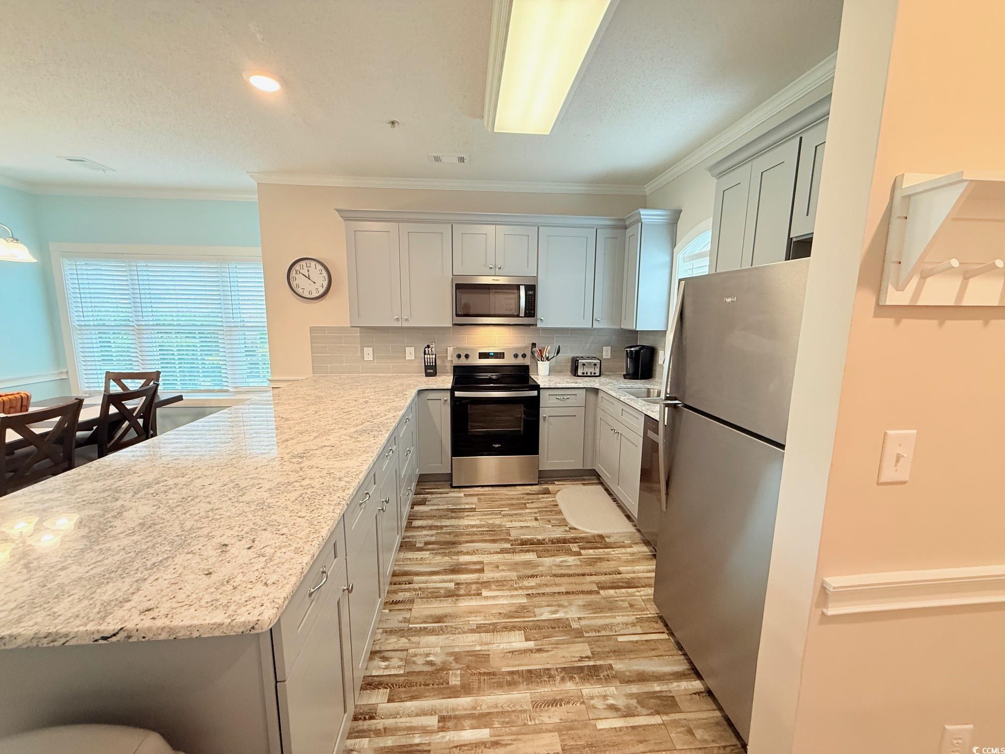 4860 Carnation Circle, Unit 17105 Myrtle Beach, SC 29577 - Photo 3 of 29 Kitchen with stainless steel appliances, crown molding, a peninsula, light stone counters, and light wood-style floors