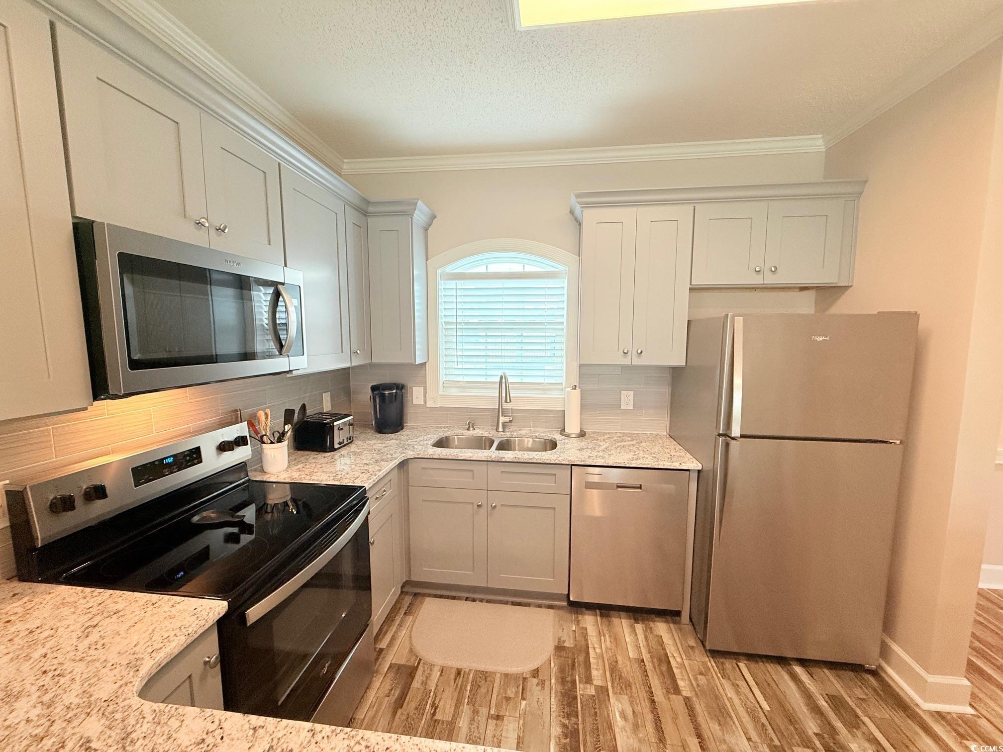 4860 Carnation Circle, Unit 17105 Myrtle Beach, SC 29577 - Photo 5 of 29 Kitchen featuring stainless steel appliances, backsplash, light stone counters, ornamental molding, and light wood-type flooring