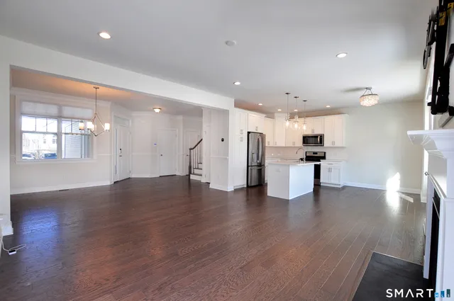 a view of an empty room with wooden floor and a kitchen