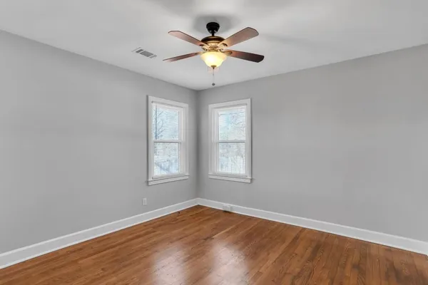 an empty room with wooden floor chandelier fan and windows