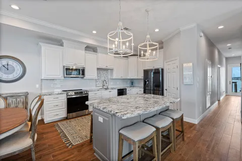 a kitchen with stainless steel appliances granite countertop a stove top oven a refrigerator a sink dishwasher a dining table and chairs with wooden floor