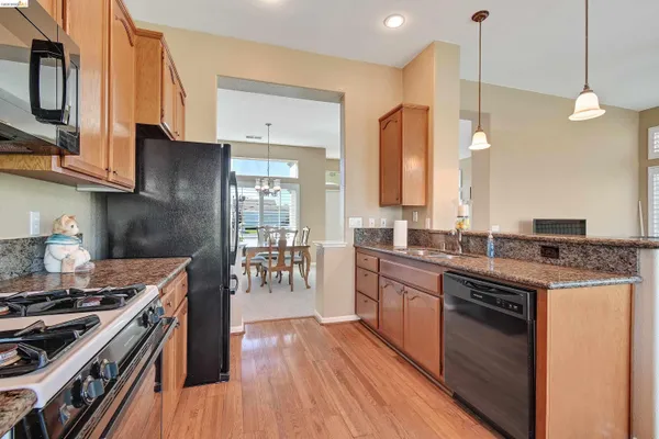 a kitchen with stainless steel appliances granite countertop a stove a sink dishwasher and a refrigerator with wooden floor