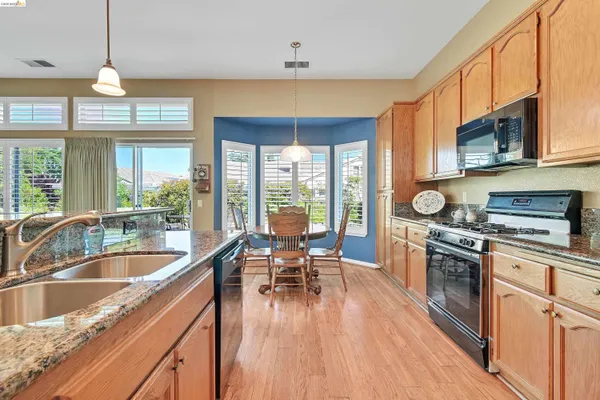 a kitchen with stainless steel appliances granite countertop a stove top oven a kitchen island a dining table and chairs with wooden floor