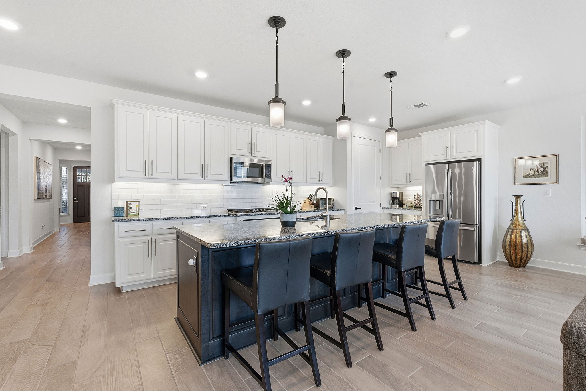 18917 Grape Seed Cove Austin, TX 78738 - Photo 19 of 33 Kitchen with dark stone countertops, hanging light fixtures, light wood-style flooring, a kitchen breakfast bar, and two tone cabinetry