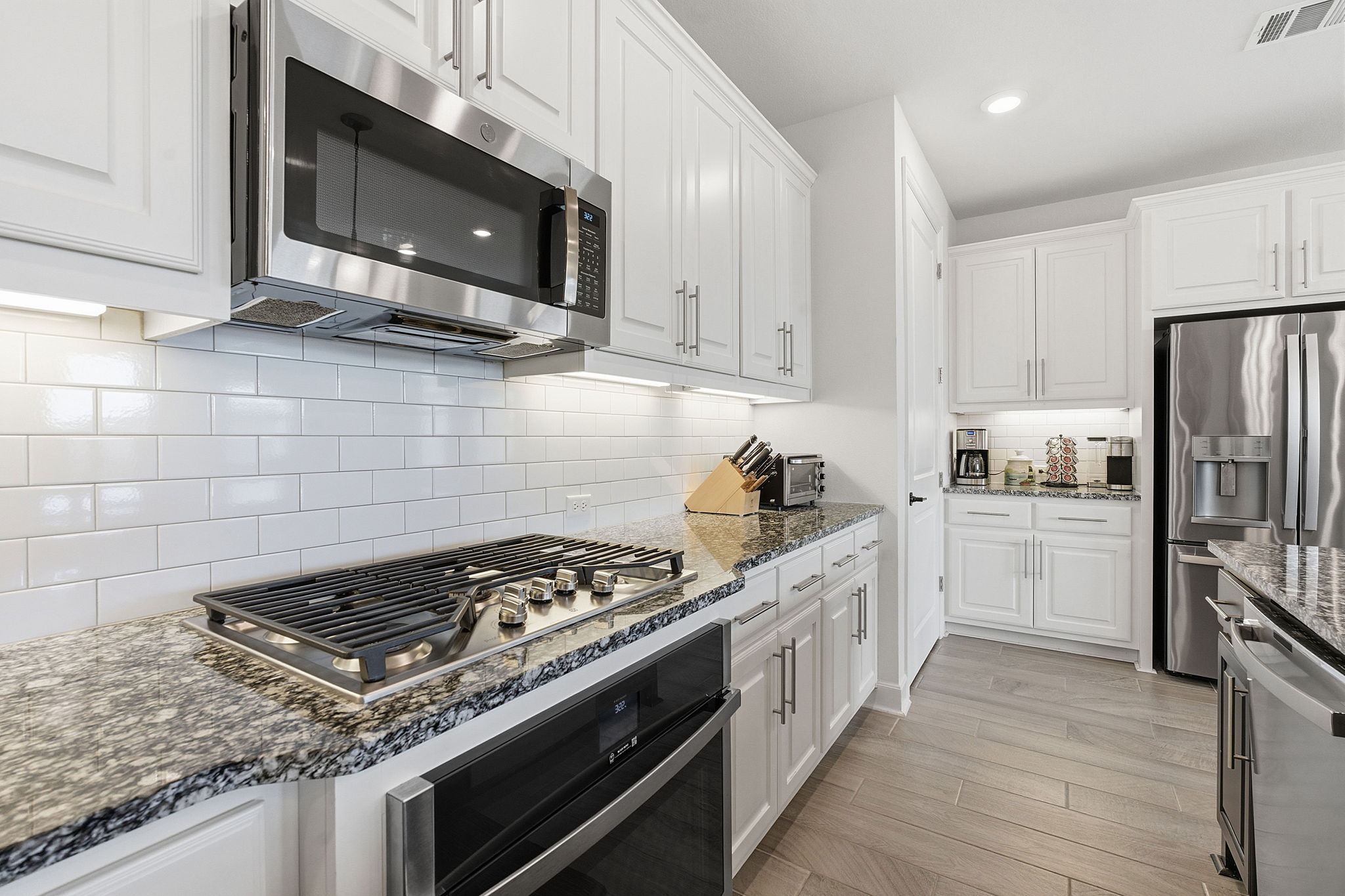 18917 Grape Seed Cove Austin, TX 78738 - Photo 20 of 33 Kitchen with white cabinetry, dark stone countertops, stainless steel appliances, decorative backsplash, and light wood-type flooring