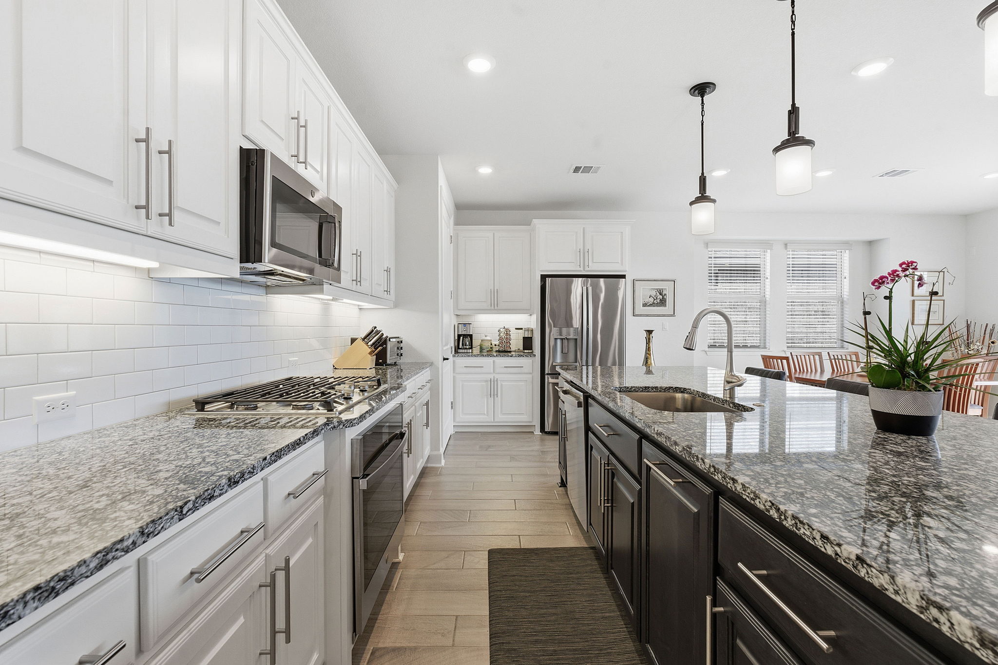 18917 Grape Seed Cove Austin, TX 78738 - Photo 6 of 33 Kitchen featuring dark stone countertops, hanging light fixtures, two tone cabinets, stainless steel appliances, and light wood-style floors