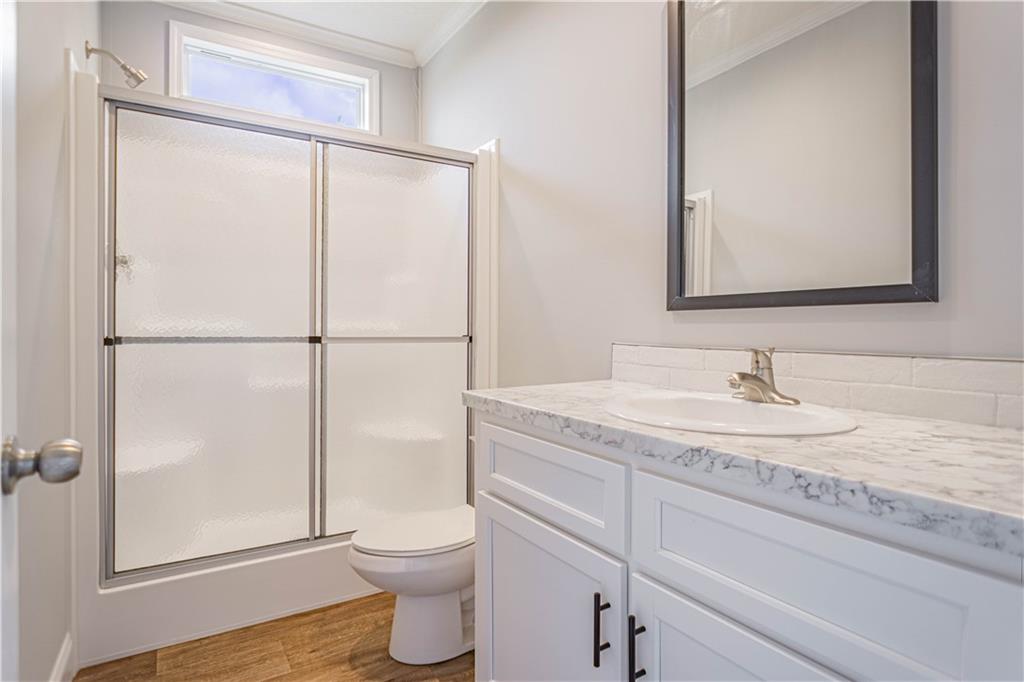 210 Ridge Road Seale, AL 36875 - Photo 13 of 16 Spa-inspired bathroom featuring a frameless glass shower enclosure with chrome hardware, white cabinetry with brushed nickel pulls, marble-look countertop with integrated sink, and wood-finish flooring throughout