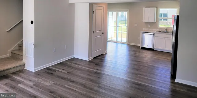 an empty room with wooden floor and a kitchen