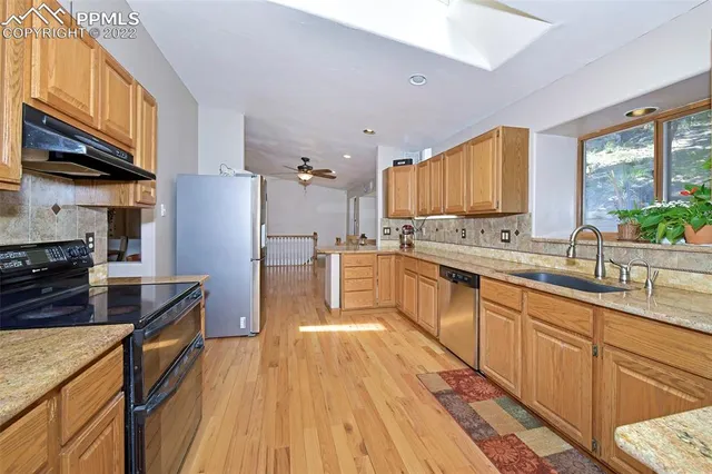 a kitchen with stainless steel appliances granite countertop a refrigerator a sink dishwasher a stove and white countertops with wooden floor