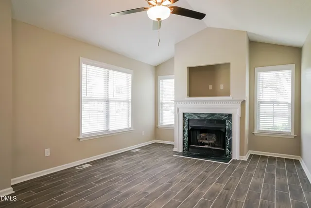 a view of an empty room with wooden floor fireplace and a window