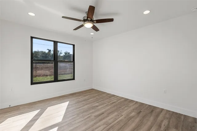 an empty room with wooden floor fan and windows